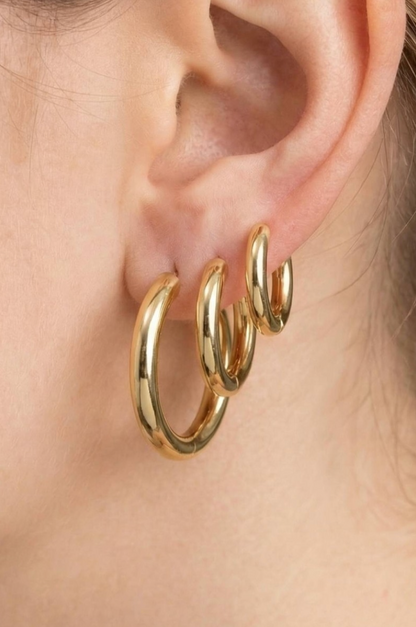 Gold hoop earrings worn on an ear with a plain background