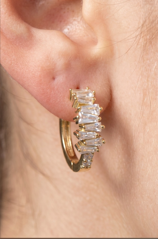 Gold mismatched huggie earrings featuring staggered baguette cubic zirconia stones and a polished brass finish.