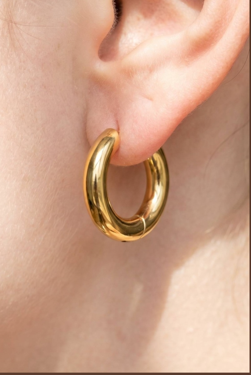 Polished gold chunky stainless steel huggie hoop earrings with a thick rounded design.