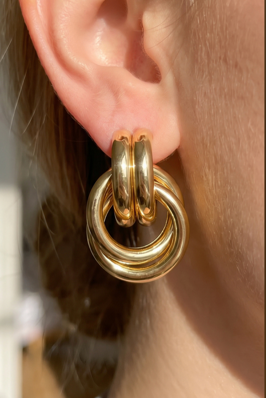 Gold-dipped triple-link doorknocker earrings featuring polished interlocking rings and oval huggie-style studs.