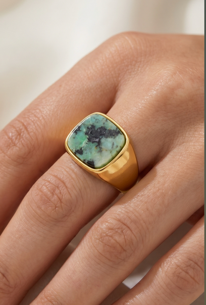 Gold-tone stainless steel signet ring with a square green natural stone centerpiece worn on a hand.