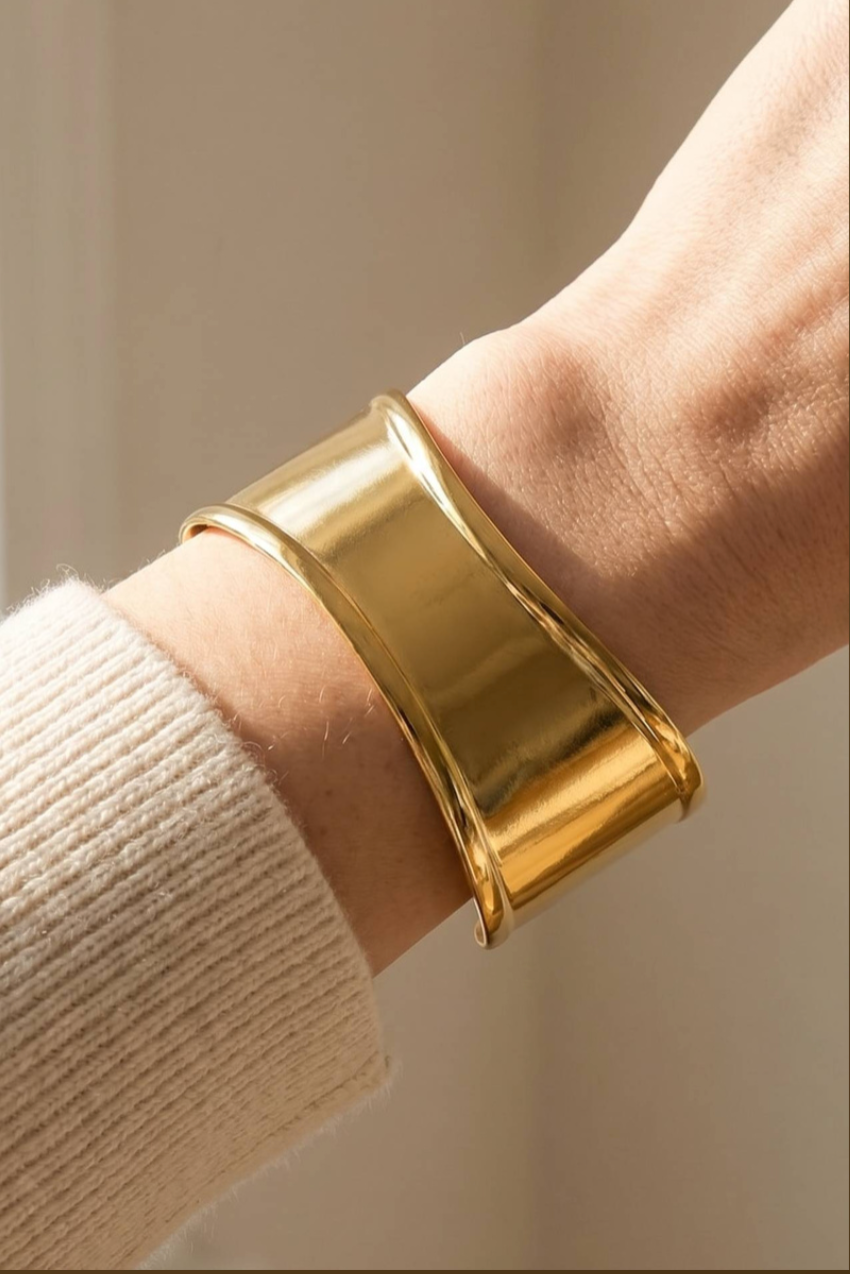 Wide polished gold stainless steel cuff bracelet with an open design and smooth architectural silhouette.