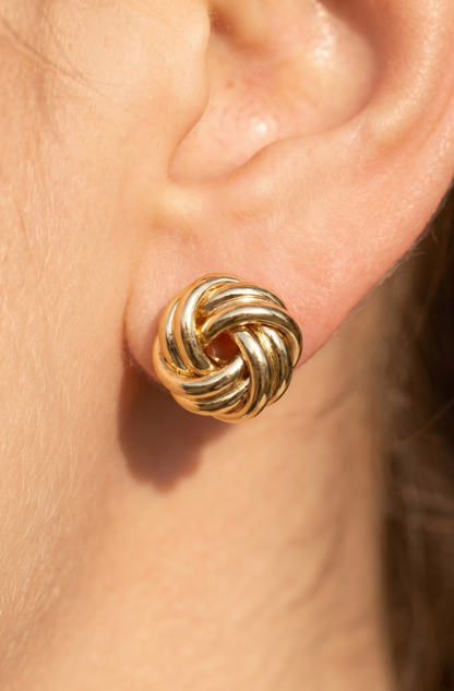 Gold-dipped braided knot stud earrings with a polished finish on a black display card.