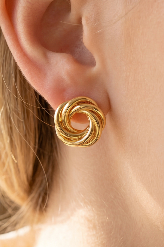 Gold-dipped open swirl knot stud earrings with a polished pinwheel design displayed on a black jewelry card.
