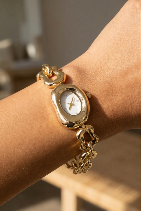 Gold abstract link bracelet watch with an oval white dial and cubic zirconia hour markers on a model's wrist.