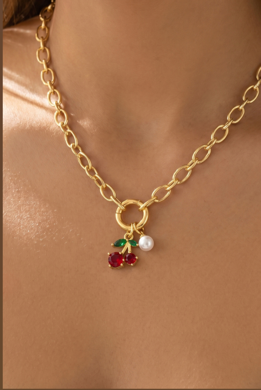 Gold oval Figaro chain necklace featuring red glass cherry charms, green leaf accents, and a pearl drop pendant.