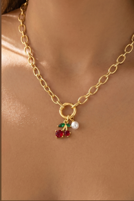 Gold oval Figaro chain necklace featuring red glass cherry charms, green leaf accents, and a pearl drop pendant.