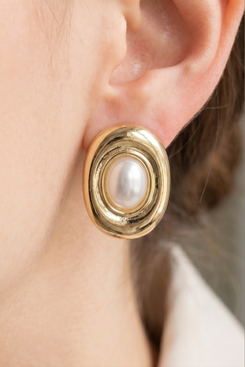 Gold oval stud earrings featuring a centered acrylic pearl with polished concentric frame detailing.