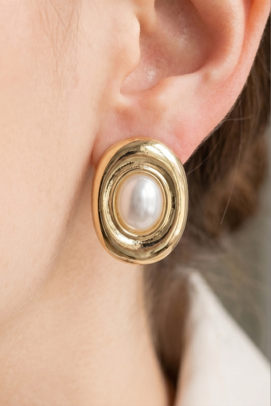 Gold oval stud earrings featuring a centered acrylic pearl with polished concentric frame detailing.