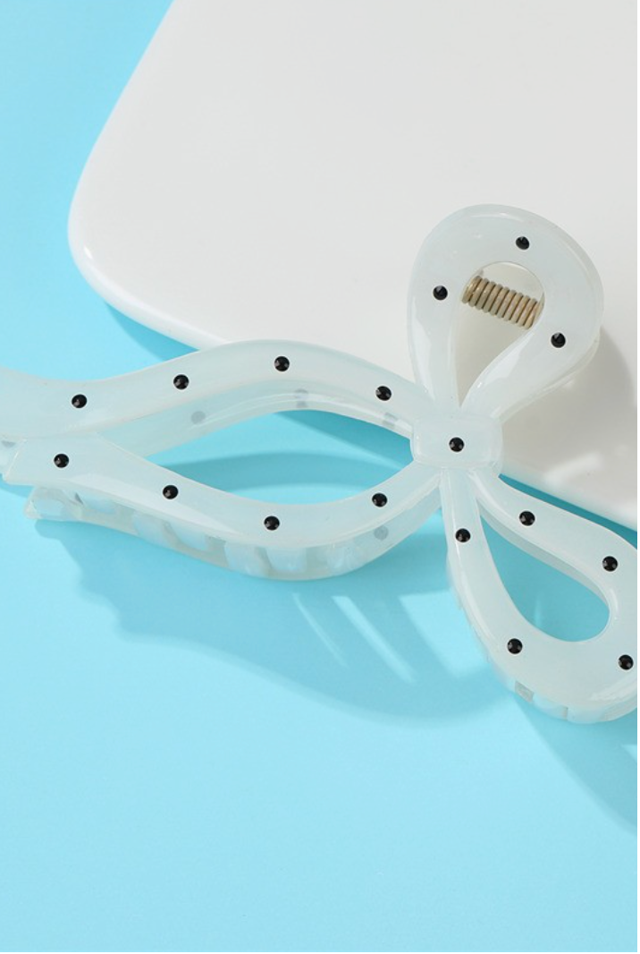 Off-white bow-shaped hair claw clip with black polka dot accents and secure claw design.