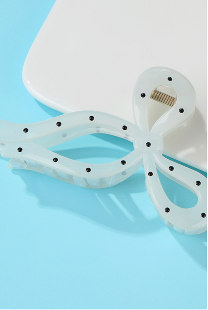 Off-white bow-shaped hair claw clip with black polka dot accents and secure claw design.