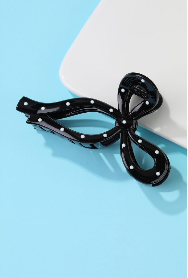 Black bow-shaped hair claw clip with white polka dot accents and secure claw design.