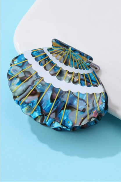 Iridescent blue marbled seashell-shaped acetate hair claw clip with gold ridged detailing.