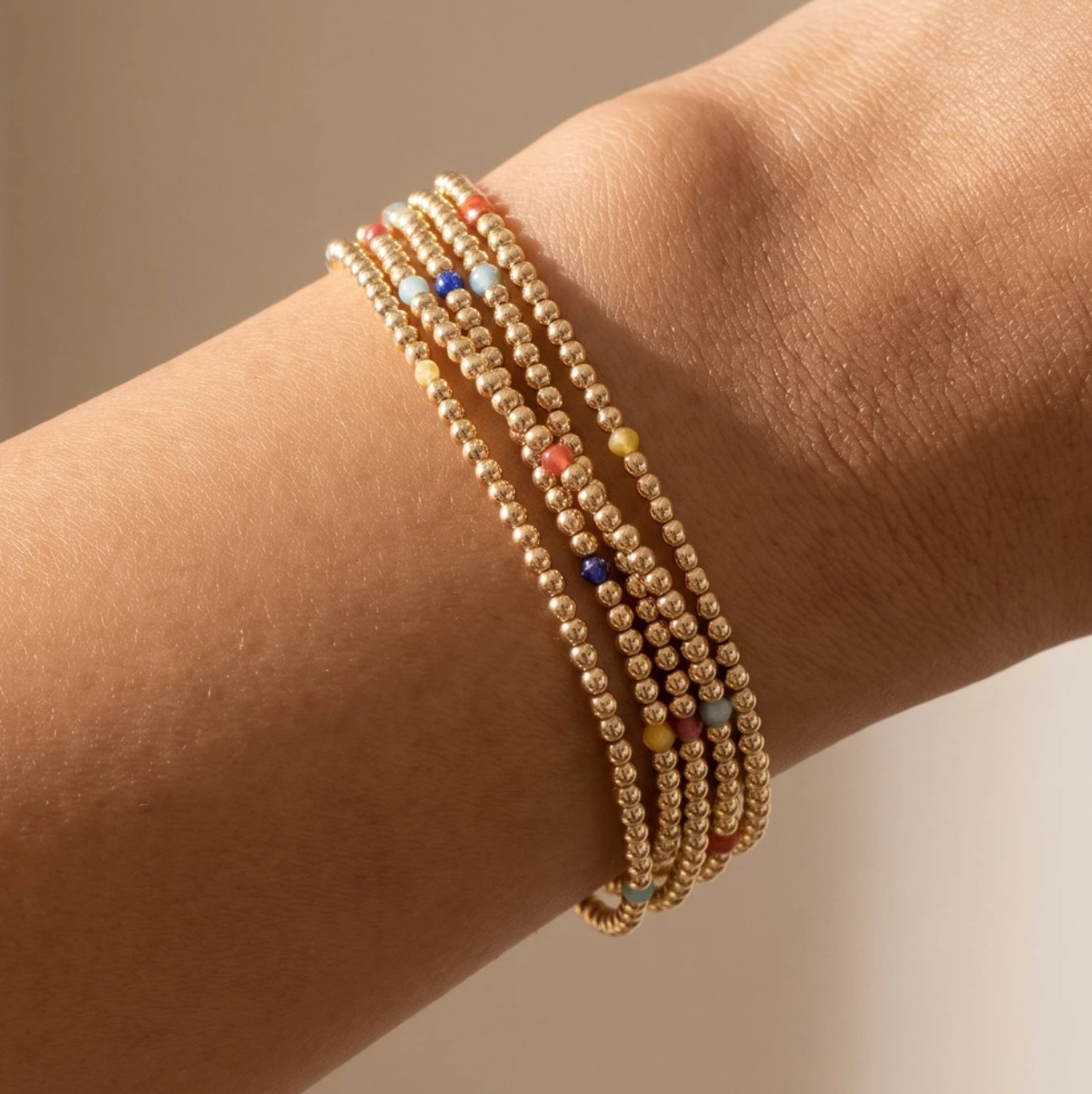 Set of gold beaded stretch bracelets with colorful faceted glass bead accents layered on the wrist.