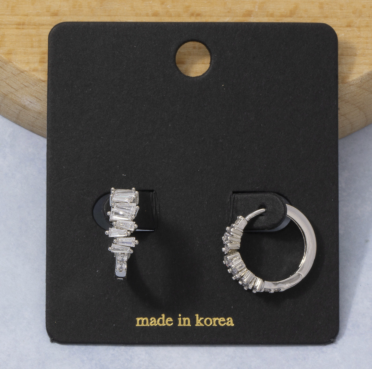 Silver mismatched huggie earrings featuring one polished hoop and one staggered baguette cubic zirconia hoop.