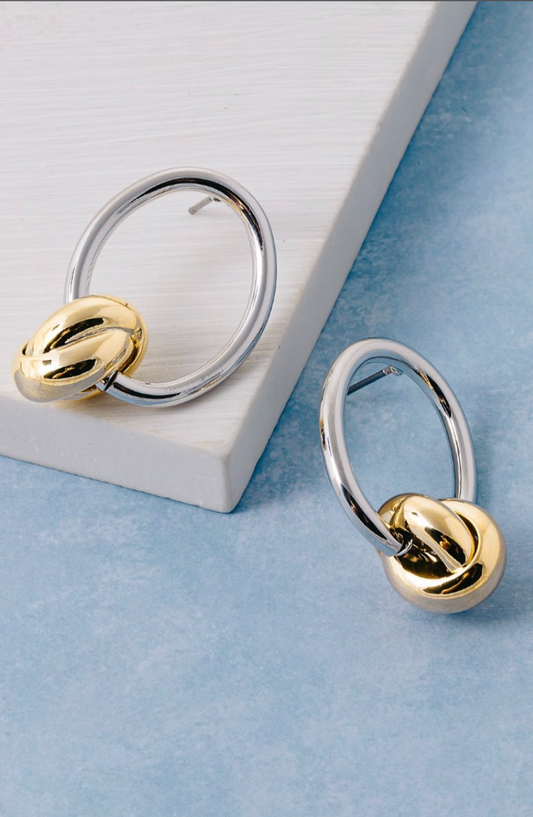 Gold knot charm earrings with polished silver oval hoops in a modern mixed-metal design.