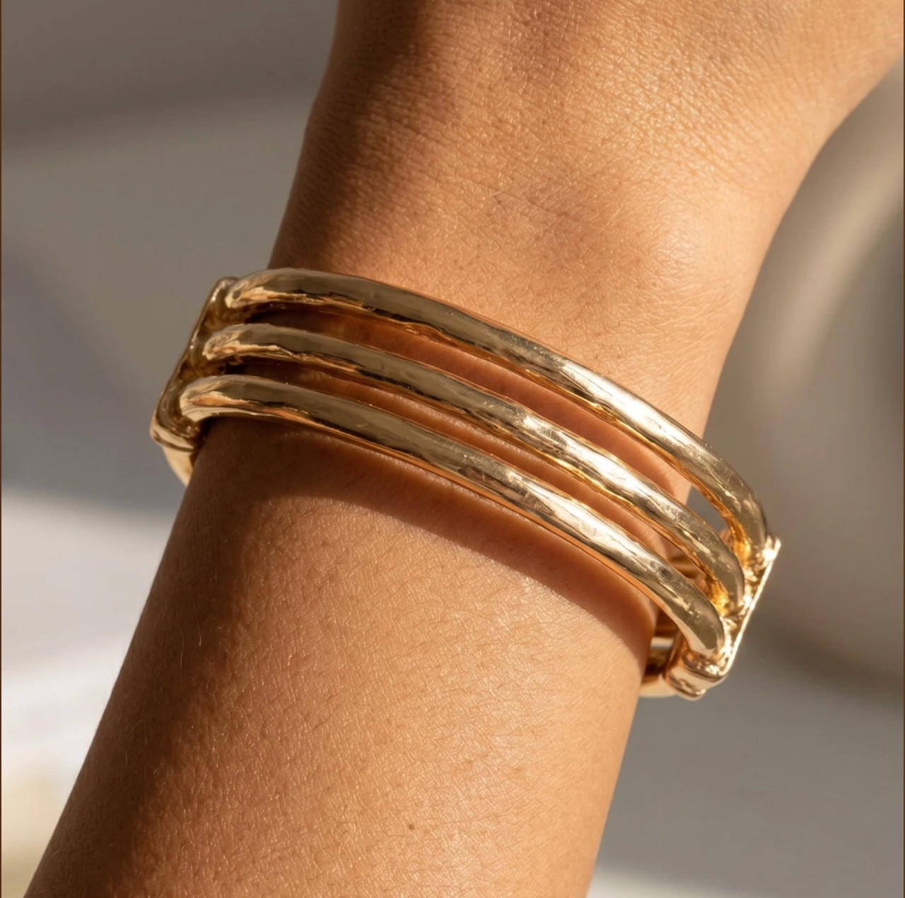 Gold hammered triple-bar cuff bracelet with an open hinged design worn on the wrist.