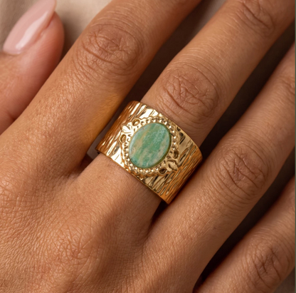 Gold-tone stainless steel ring with a textured band featuring an oval green cabochon stone surrounded by a beaded halo and leaf accents.