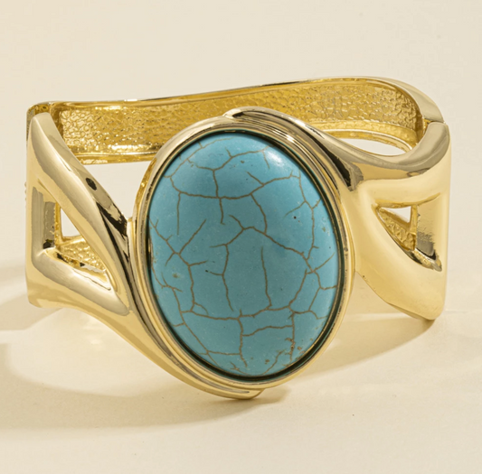 Gold-tone cuff bracelet with a large turquoise-inspired oval cabochon stone and sculptural open-loop design.