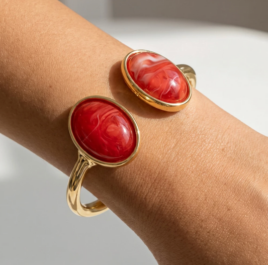 Gold-tone hinged cuff bracelet with two marbled red oval cabochon stone accents.