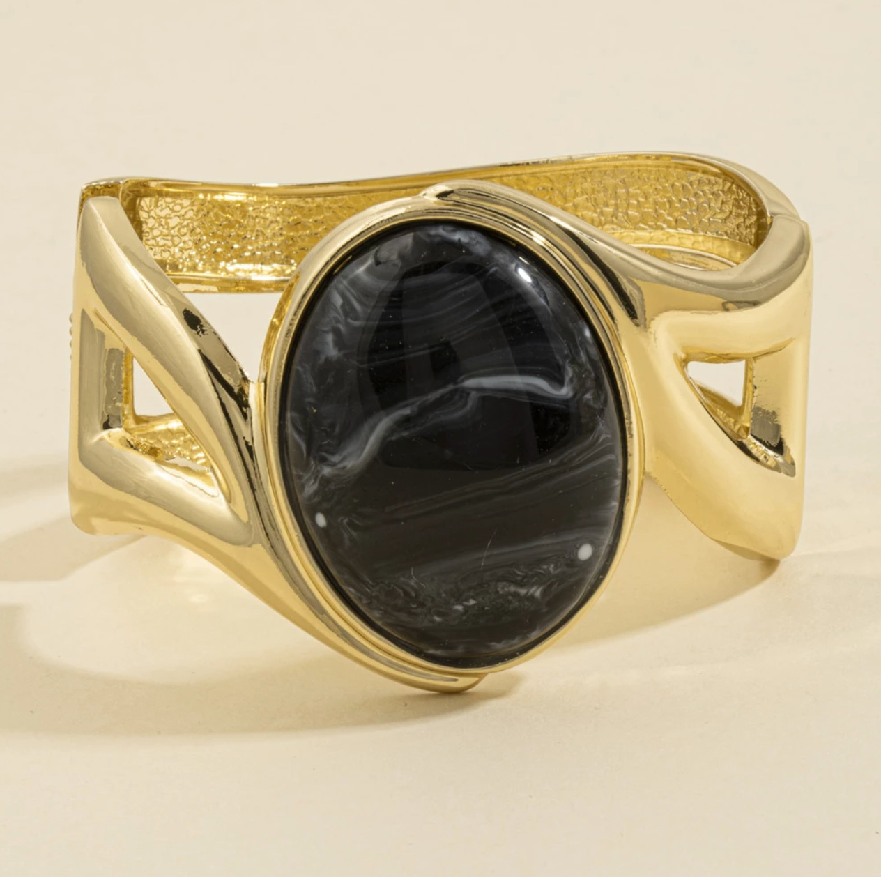 Gold-tone cuff bracelet with a large marbled black oval stone and sculptural open-band design.