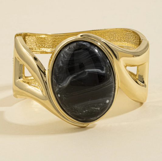 Gold-tone cuff bracelet with a large marbled black oval stone and sculptural open-band design.