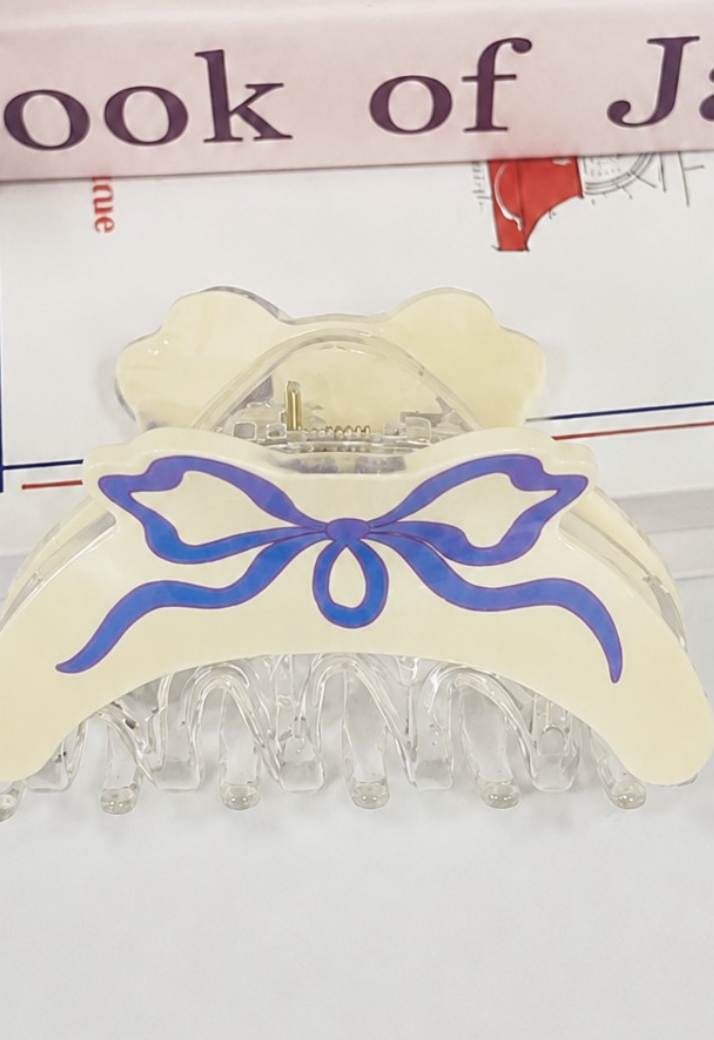 Off-white coquette hair claw clip with blue illustrated ribbon bow and clear resin teeth.