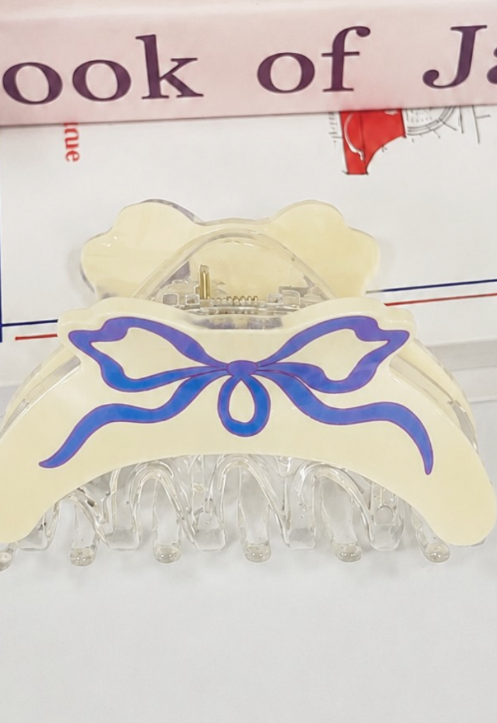 Off-white coquette hair claw clip with blue illustrated ribbon bow and clear resin teeth.