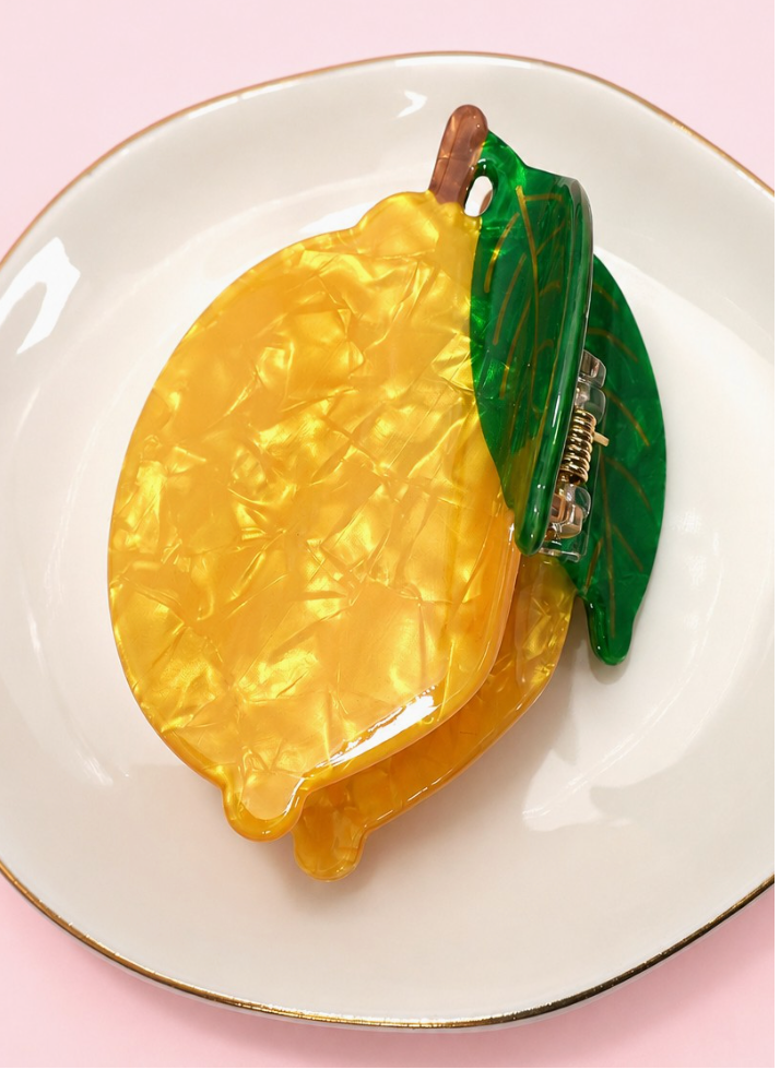 Zesty Claw Clip Lemon featuring a glossy marbled yellow lemon design with dimensional green leaves and brown stem detail.