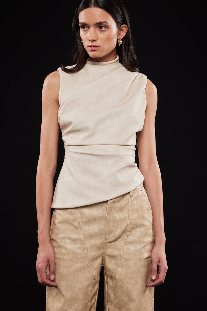 Woman wearing a beige sleeveless top and pants against a black background