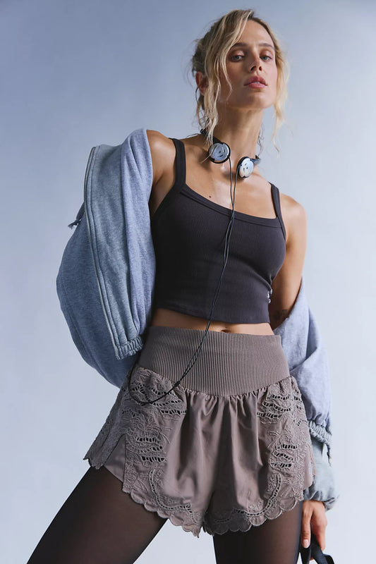 Woman in athletic wear with a gray jacket over her shoulder against a light blue background