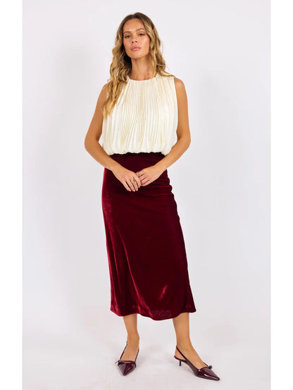 Woman wearing a white top and burgundy velvet skirt on a light gray background