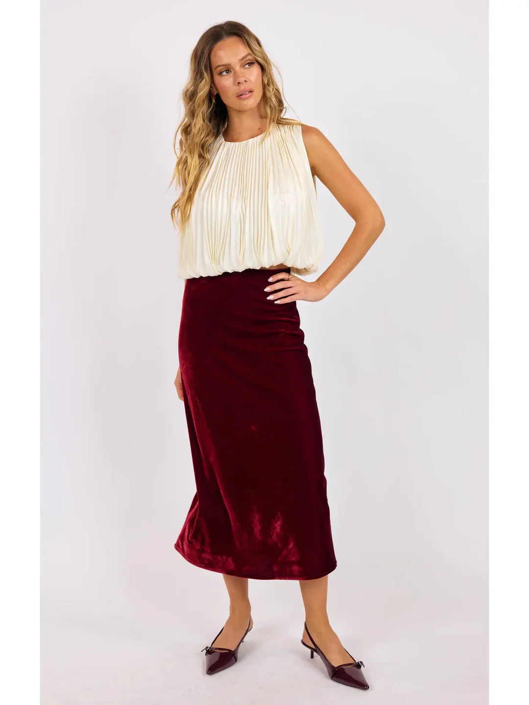 Woman wearing a white blouse and burgundy velvet skirt on a light gray background