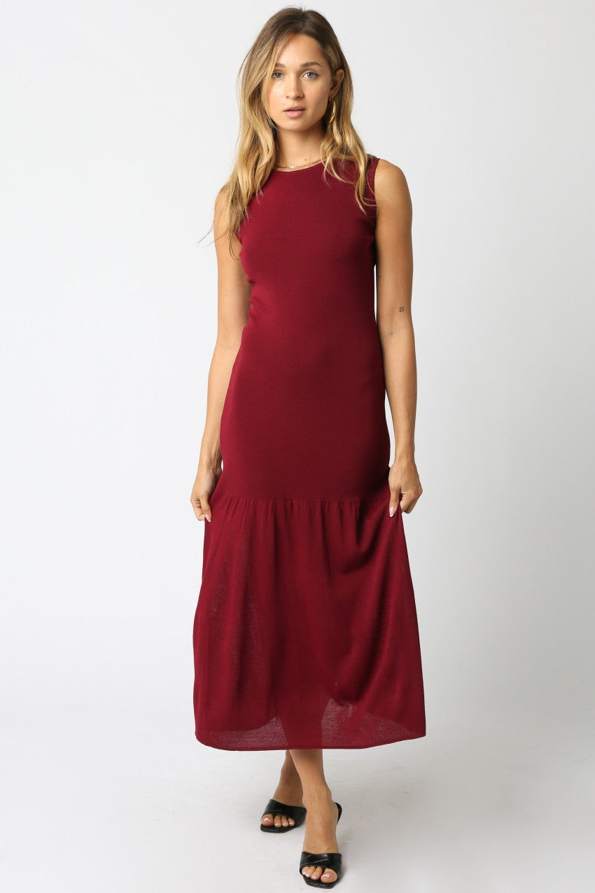Woman wearing a sleeveless maroon knit maxi dress with a flounce hem and fitted bodice styled with black heels.