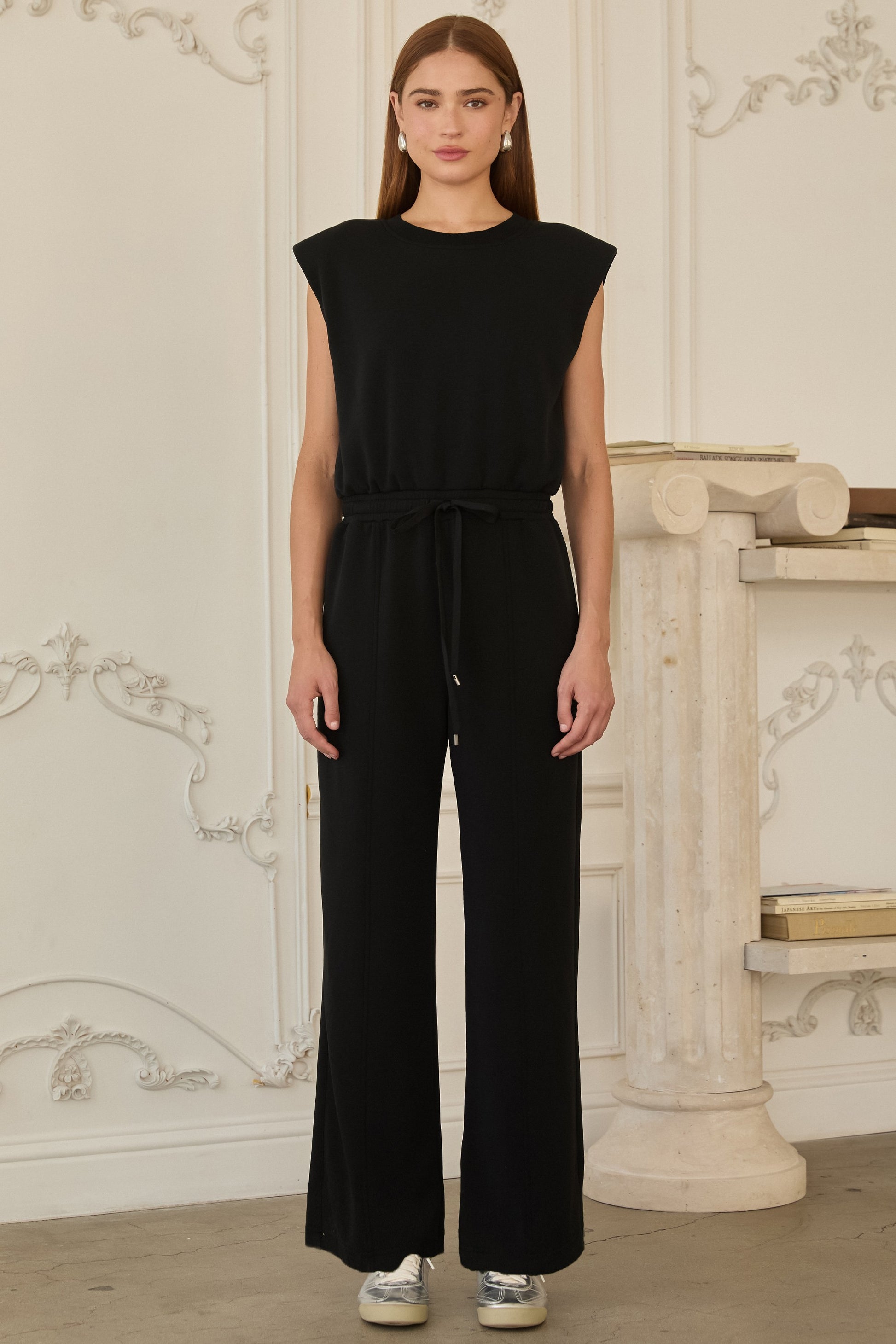 Model wearing black sleeveless brushed modal jumpsuit with structured shoulders, drawstring waist, and wide-leg fit.