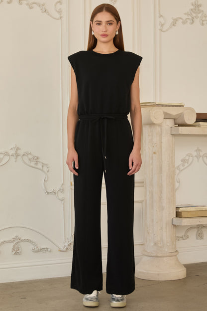 Model wearing black sleeveless brushed modal jumpsuit with structured shoulders, drawstring waist, and wide-leg fit.