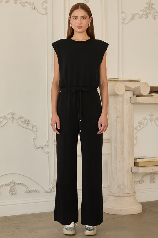Model wearing black sleeveless brushed modal jumpsuit with structured shoulders, drawstring waist, and wide-leg fit.