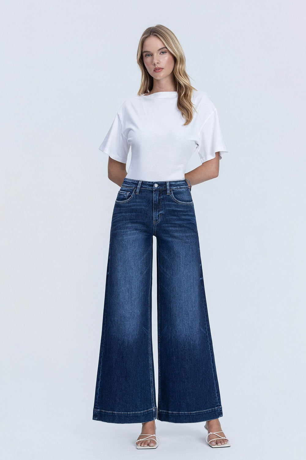 Woman wearing a white t-shirt and blue wide-leg jeans on a light gray background