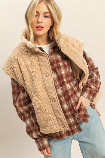 Model wearing beige sherpa vest with snap button placket, tie-up side details, and cap-sleeve effect layered over plaid shirt.