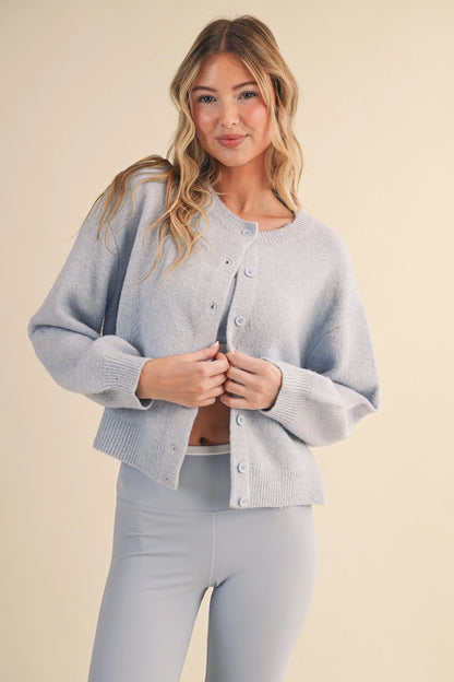 Model wearing a light blue knit button-up cardigan sweater with a relaxed fit