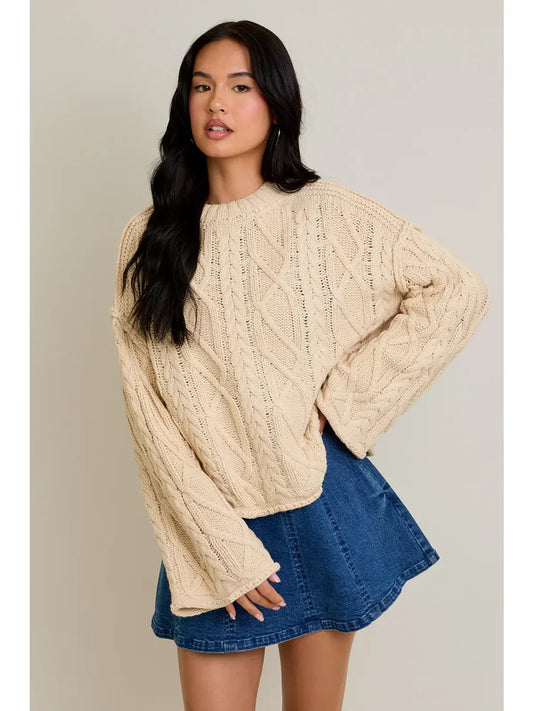 Neutral oversized cable knit sweater with crew neckline and relaxed sleeves styled with a denim mini skirt.