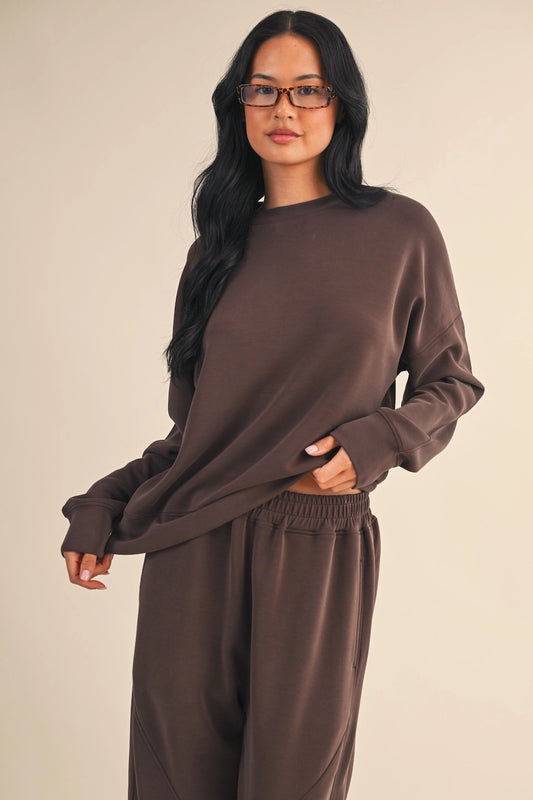 Woman wearing oversized brown air scuba sweatshirt with relaxed fit and dropped shoulders.