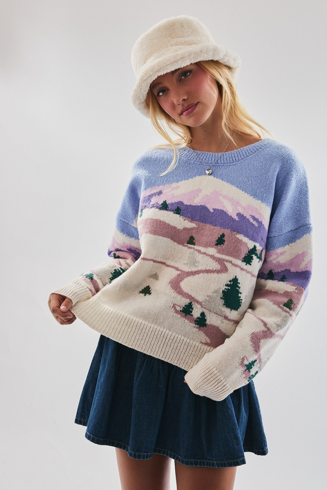 Model wearing mountain landscape knit sweater in pastel blue, cream, and lilac tones with denim mini skirt