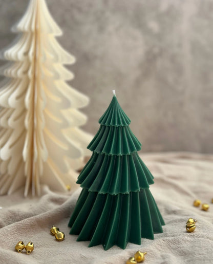 Green tree-shaped candle with gold jingle bells on a textured surface