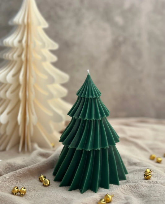 Green tree-shaped candle with gold jingle bells on a textured surface