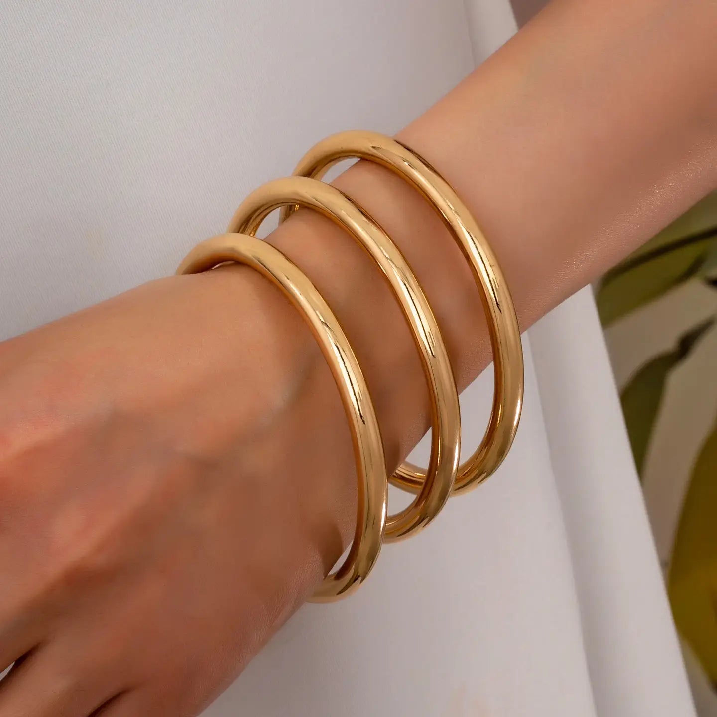 Gold bangles on a wrist against a neutral background