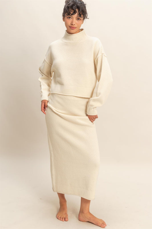 Model wearing ivory textured knit sweater and matching midi skirt set with high neckline and relaxed fit.