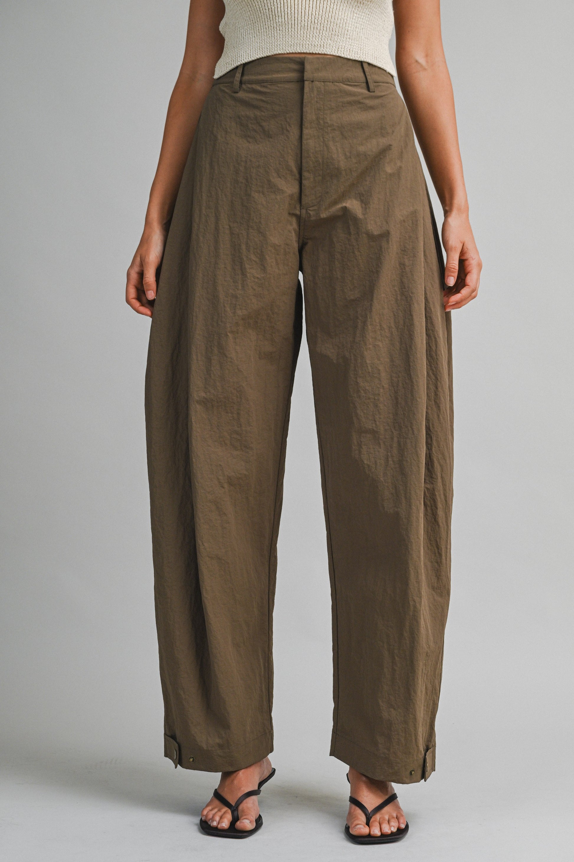 Model wearing high-waisted barrel pants with a structured curved silhouette and adjustable hem tabs