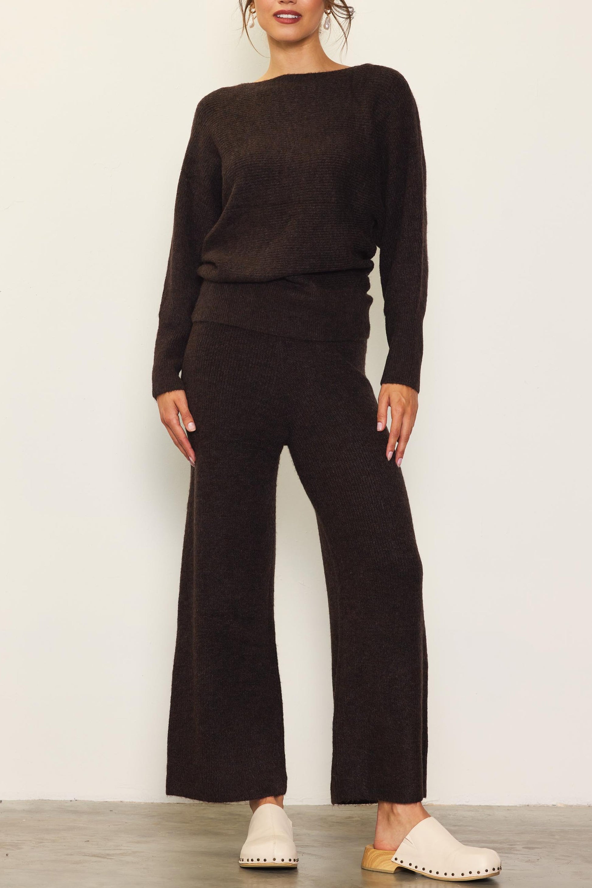 Model wearing chocolate brown off-shoulder rib-knit sweater with relaxed fit and long sleeves.