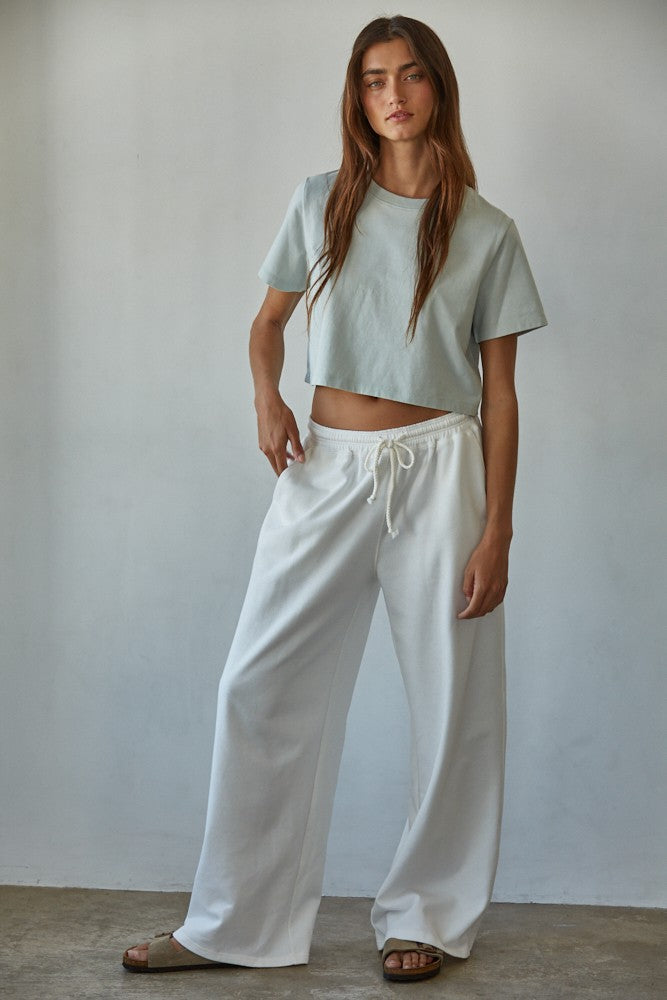 Woman wearing pale blue cropped cotton tee with wide-leg white drawstring pants and slide sandals